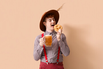 Young man in traditional German clothes with beer eating pretzel on beige background