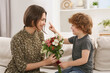 © New Africa - Little son congratulating his mom with Mother`s day at home. Woman holding bouquet of flowers