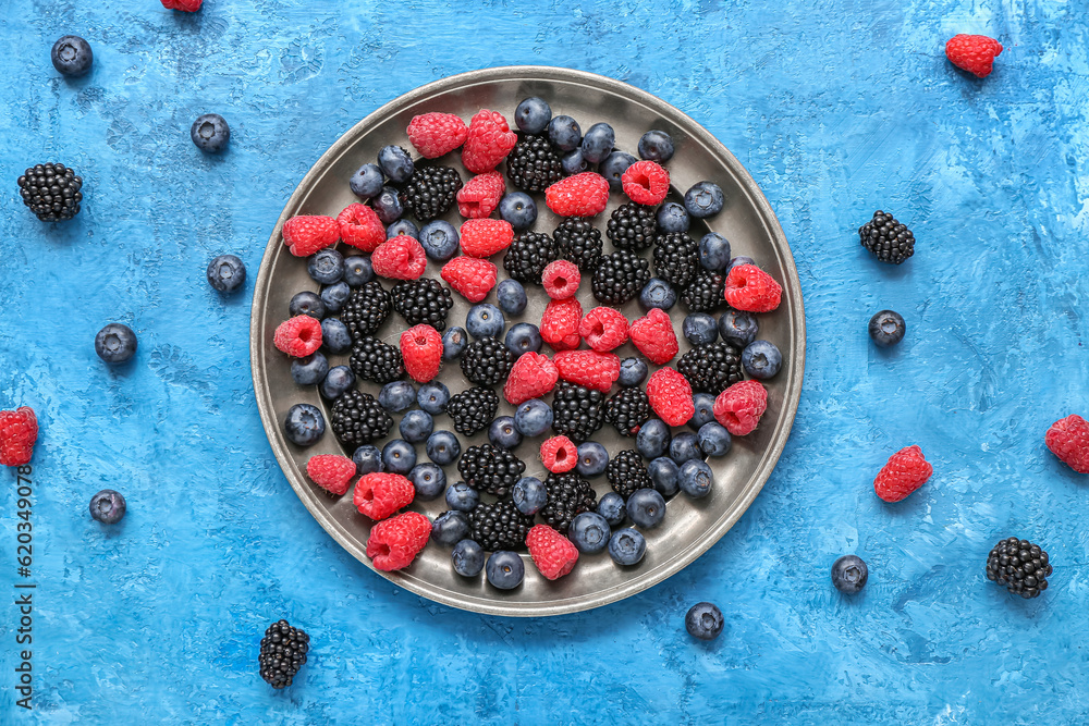Plate with different fresh berries on blue background
