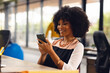 © Wavebreak Media - Happy african american businesswoman sitting at desk and using smartphone at office