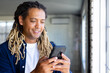 © Wavebreak Media - Happy biracial casual businessman with dreadlocks using smartphone by window in sunny office