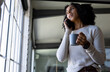 © Wavebreak Media - Biracial casual businesswoman with coffee talking on smartphone standing in office, copy space