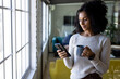 © Wavebreak Media - Happy biracial casual businesswoman with coffee using smartphone standing in office, copy space