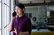 © Wavebreak Media - Happy asian casual businesswoman standing next to window in office talking on smartphone, copy space