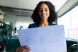 © Wavebreak Media - Happy biracial casual businesswoman in office having video call, holding document and smiling