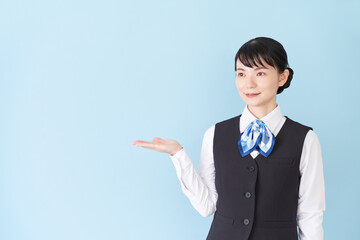 手で案内するベストにリボンタイの制服を着た、受付業務、事務業務の女性