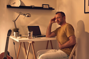 Wall Mural - Man with stomach pain and headache while working at home on a laptop.