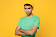 © ViDi Studio - Side view young sad frowning upset man of African American ethnicity he wears casual clothes green t-shirt hat hold hands crossed isolated on plain yellow background studio portrait Lifestyle concept
