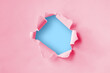 © Nitiphol - Torn hole in plain pink paper with a blue background. Concept for advertising.