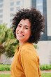 © Jose Calsina - Vertical individual portrait of hispanic young adult woman with curly hair and white teeth smiling looking at camera with carefree and friendly expression. Cool cheerful female standing outside. High