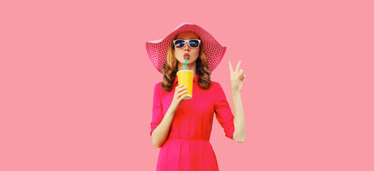 summer portrait of beautiful young woman drinking fresh juice wearing straw hat, pink dress on backg