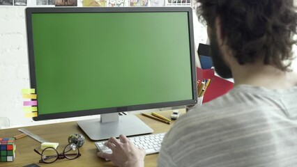 Green screen computer display placed on wooden table in working room. Adult caucasian male working in front of monitor. Typing on the keyboard while writing code, text, copywriting, chatting.