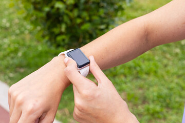 Cropped shot of a young woman checking a sport smartwatch after running outdoors. Female wearing a fitness tracker watch to monitor training in an urban park. Wellness, health and active lifestyle.