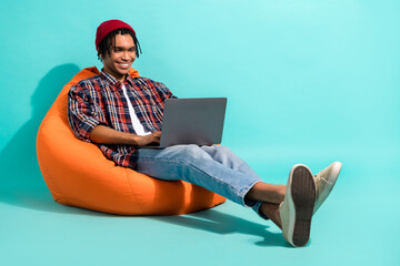 Poster - Full size photo of intelligent guy dressed checkered shirt jeans sit on pouf typing email on laptop isolated on teal color background