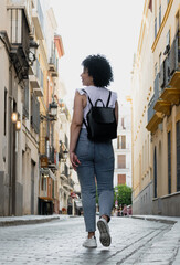 Cuban young woman with afro hair smiling walking down the street with a backpack. looking to the side 