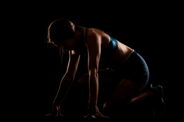 Wall Mural - Female runner silhouette in low race start position. Girl in sportswear against dark background.