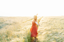 A happy young woman with raised arms relaxing in wheat field on sunset. Celebrating freedom. Positive emotions feeling life, peace of mind. Mental health practice. Nature relaxation. Selective focus.