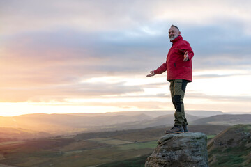 Bearded  Man in orange jacket relaxing alone on the top of  mountain  and drinking hot coffee at sunrise. Travel  Lifestyle concept The national park Peak District in England