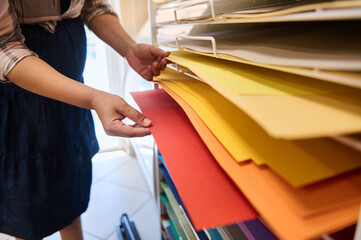 Close-up woman choosing design paper on shelves with colorful papers for ?reativity and fine art. Design occupation