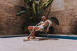 Chico joven musculado y tatuado posando  sin camiseta en piscina de estilo  boho en un hotel un dia soleado de verano