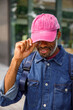 © Jovo Jovanovic/Stocksy - Man in denim jacket holding visor of his pink cap on a sunny day
