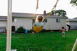 © Maria Manco/Stocksy - Sister swings on play set while brother runs away