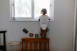 © Maria Manco/Stocksy - Toddler girl stands on back of bed to look outside