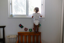 Toddler Girl Stands On Back Of Bed To Look Outside