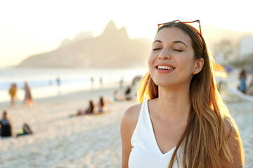 Portrait of young smiling Brazilian woman with closed eyes on Ipanema beach at sunset in Rio de Janeiro, Brazil