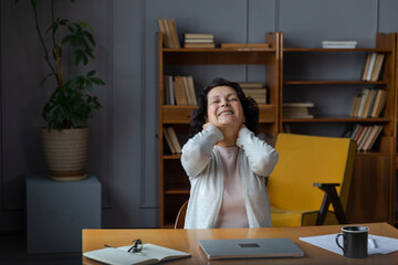 Middle aged senior woman at home relaxing stretching hands and body taking break from work on laptop. Older mature woman happy after work done satisfied by good result. Fatigue from long laptop usage