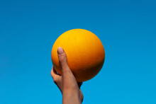 Hand Holding A Yellow Ball And Blue Sky Background
