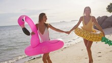 Two Girls In Love Flirt With Each Other On The Sandy Beach After Swimming In The Sea With Inflatable Circles. The Women Are Enjoying Their Vacation And Each Other's Time.
