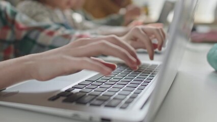 Close up impersonal shot of hands of girl typing on laptop keyboard at school desk during computer class