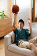 © BONNINSTUDIO/Stocksy - Man with basketball ball sitting on sofa at home