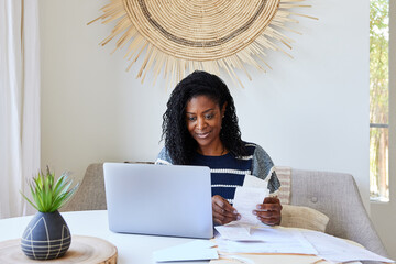 Mature Black woman looking at receipts and finances on computer