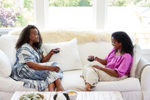 Mature Black Friends Talking Together At Home With Wine On Sofa