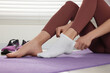 © New Africa - Woman putting on white socks on exercise mat indoors, closeup
