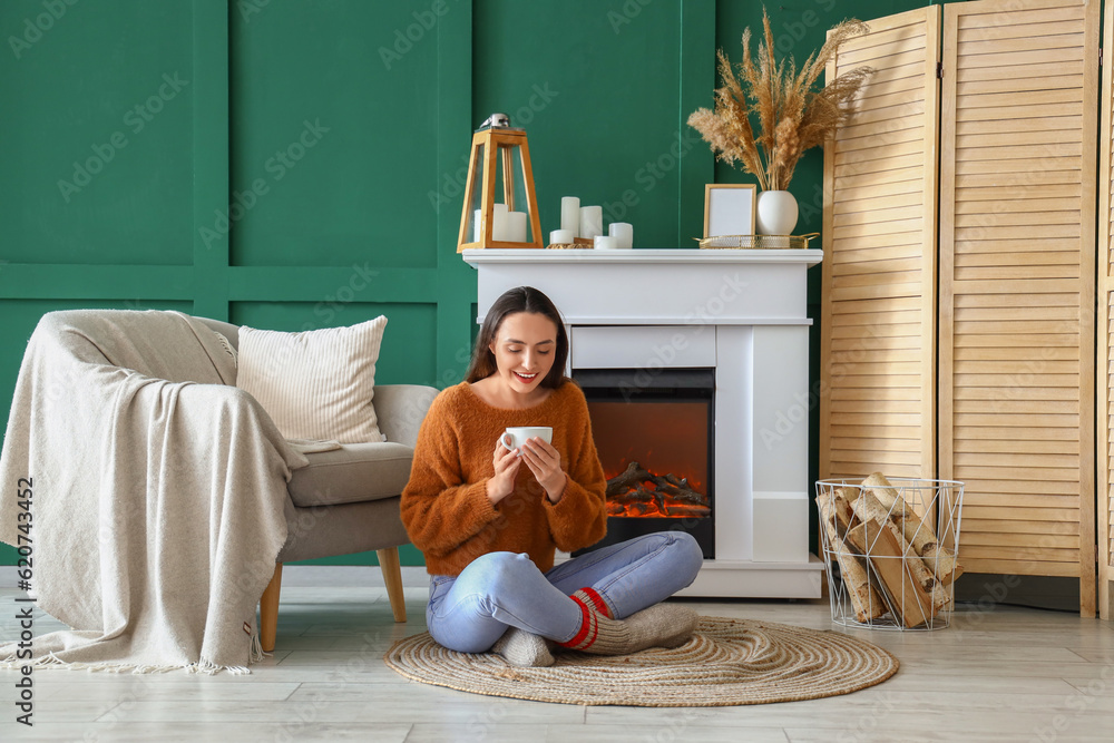 Young woman drinking hot tea near fireplace at home