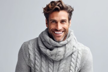 Wall Mural - Portrait of a handsome man in scarf and sweater smiling at camera over grey background