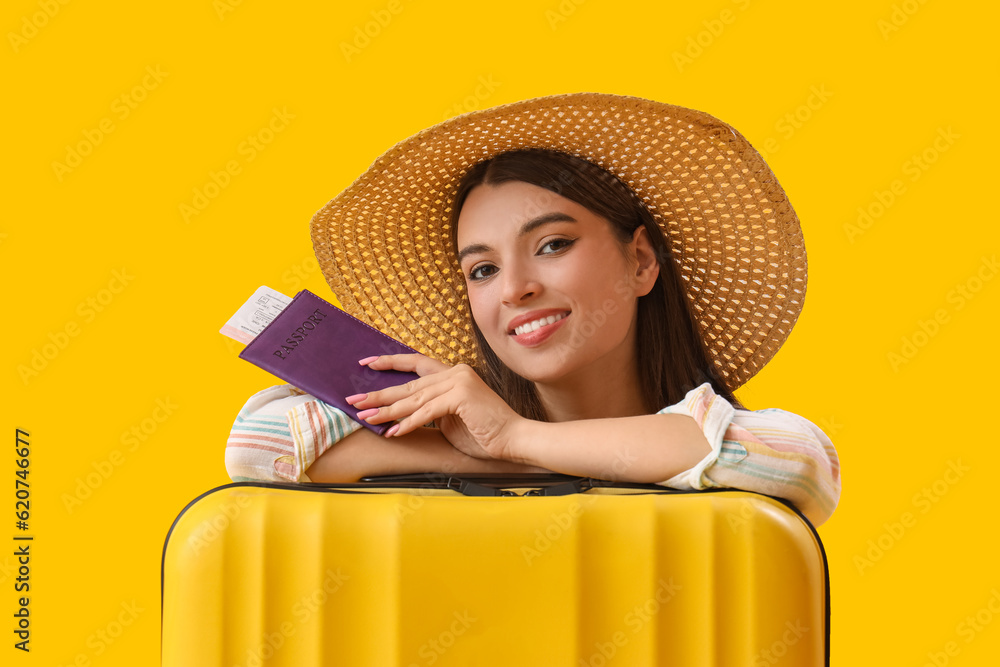 Young woman with passport and suitcase on yellow background