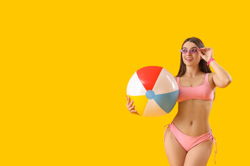 Poster - Young woman in swimsuit with beach ball on yellow background