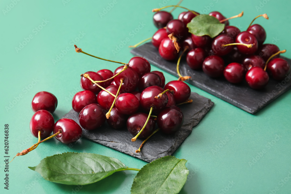 Boards with sweet cherries on green background