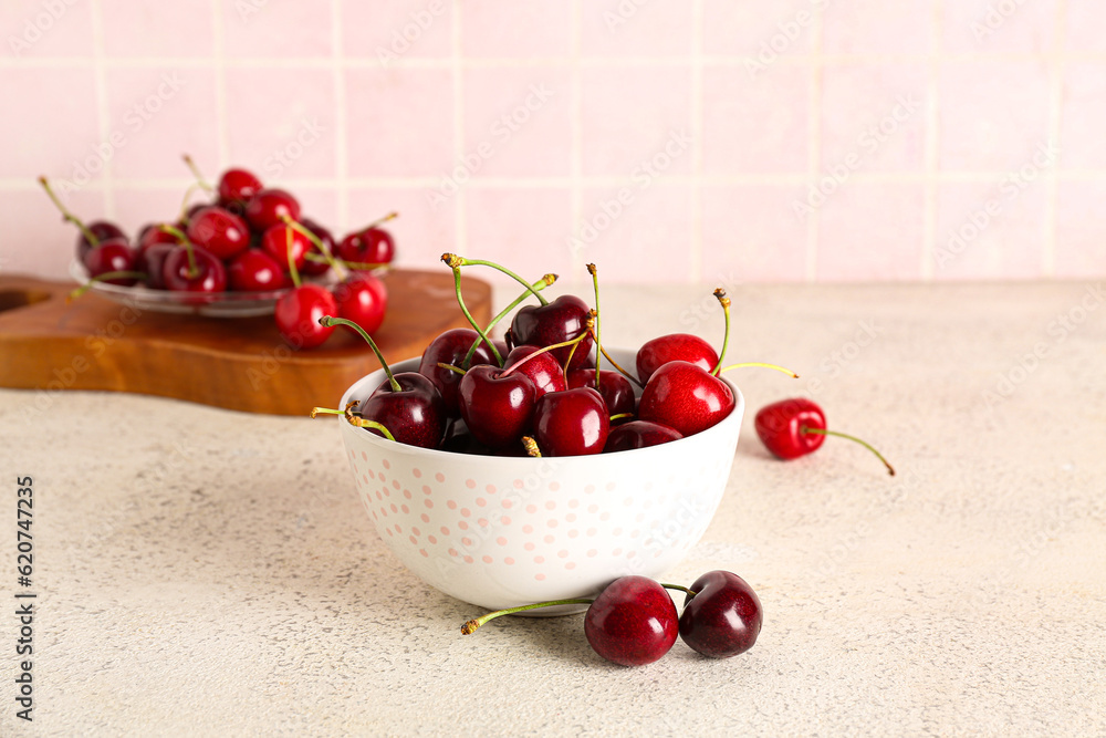 Bowl and board with sweet cherries on white table