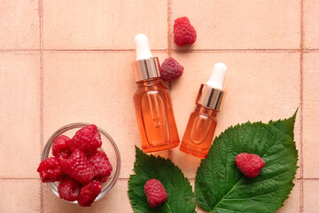 Bottles of cosmetic raspberry oil and bowl with berries on pink tile table