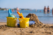 Children's Beach Toys - Buckets, Spade And Shovel On Sand On A Sunny Day. Bright Toys On The Background Of The Sea.