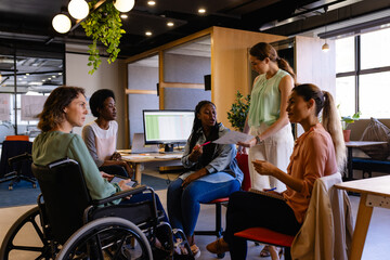 Diverse female colleagues in discussion using tablet in casual office meeting