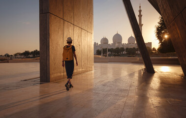 Wall Mural - travel to the United Arab Emirates, Happy young asian female traveler with backpack and hat in Wahat Al Karama or Oasis of Dignity, permanent memorial for its martyrs, and Shaikh Zayed Grand Mosque.