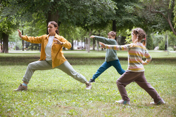 Family mom and two kids practice Tai Chi Chuan in a park.  Chinese management skill Qi's energy.