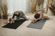 © ADDICTIVE STOCK - Flexible couple doing stretching pose on mat near curtain with sunlight