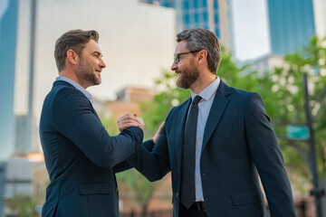 Wall Mural - Two businessmen shaking hands on city street. Business men in suit shaking hands outdoors. Handshake between two businessmen. Greeting, dealing, merger and acquisition concept.